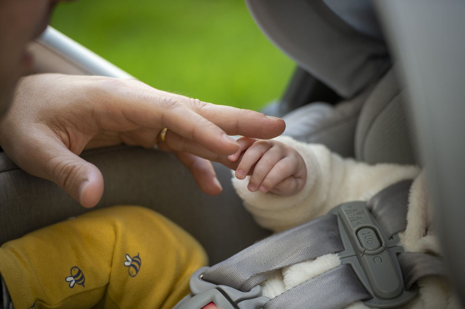 A parent's hand gently holding a baby's fingers in a car seat