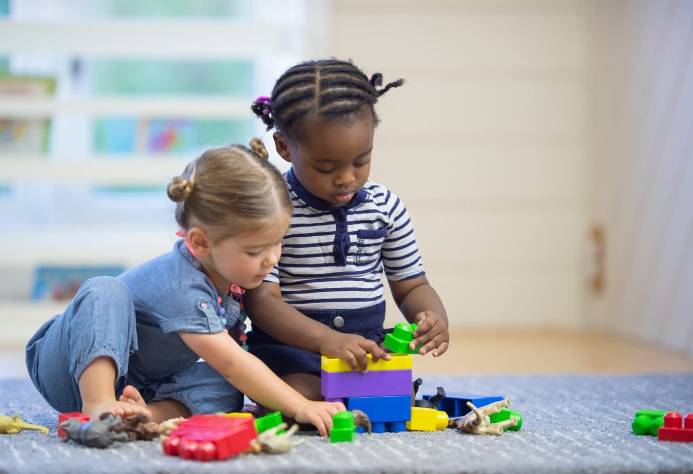 Two toddlers building with colorful blocks on a classroom floor